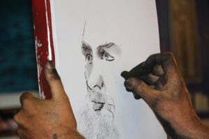 the photo is of an artist drawing a face with charcoal